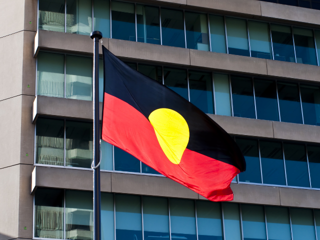 Aboriginal flag flying in front of city skyscraper.