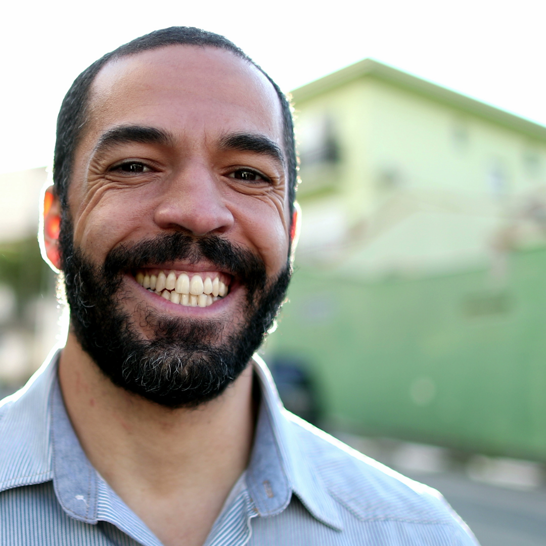 A Brazilian man wearing a blue button-up shirt smiles at the camera.