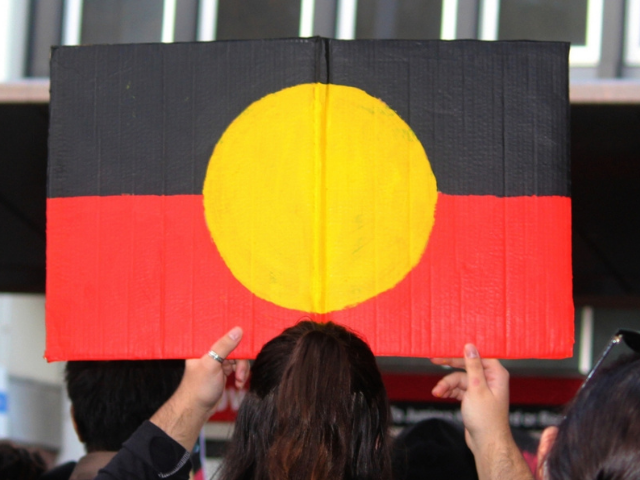 A photo of a person from behind holding an Aboriginal flag.