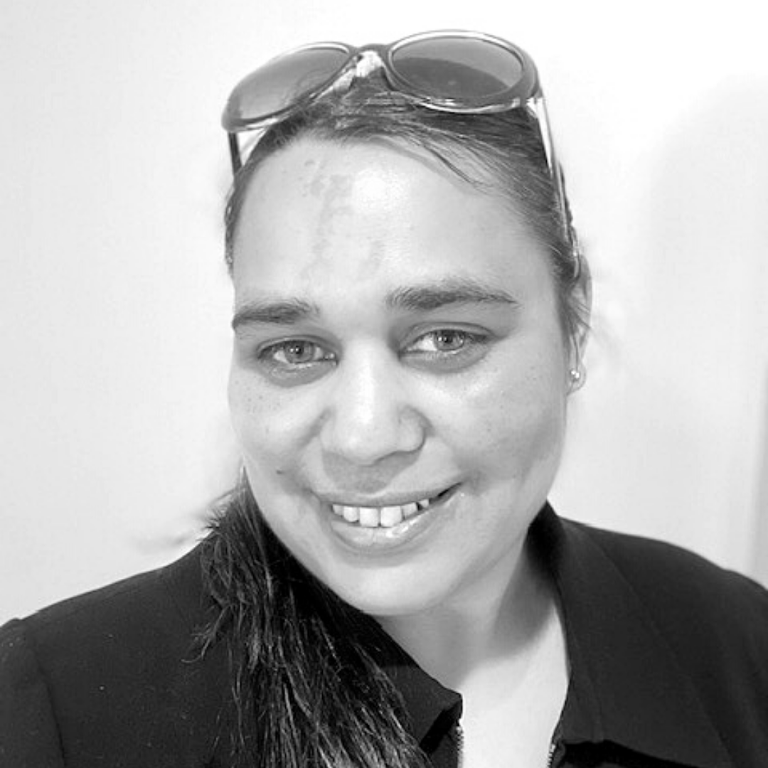 A black and white photo of Bobbi, who has long hair, is smiling at the camera and has sunglasses on her head.