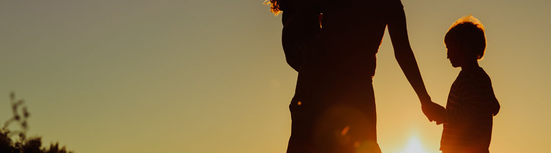 Silhouette of a person holding a child's hand at sunset.