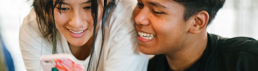 Two teenagers smiling looking at an iPhone.