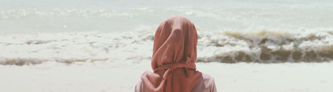 A woman with a headscarf sitting in front of the ocean.