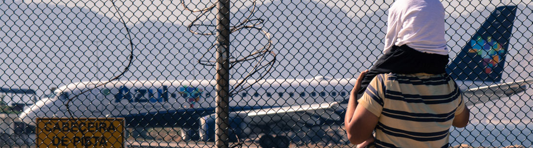 A child on the shoulders of a person at an airport fence.
