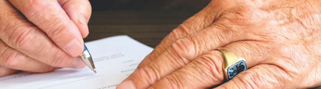 An older person signing a form. 