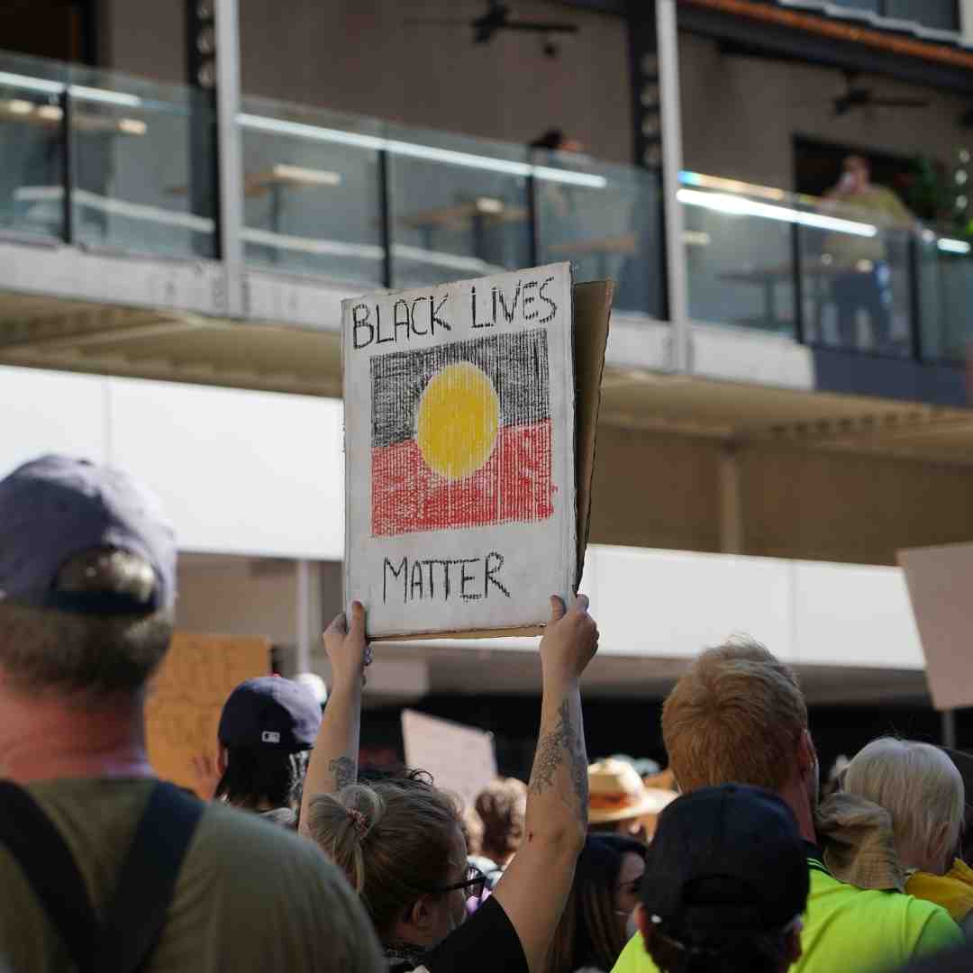 Person holds a Black Lives Matter sign with an Aboriginal flag at a protest.