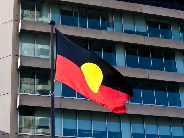 Aboriginal flag flying on a pole in front of a high rise building.