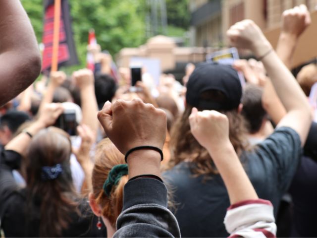 A person holds a fist up at a protest outside NSW Parliament House.