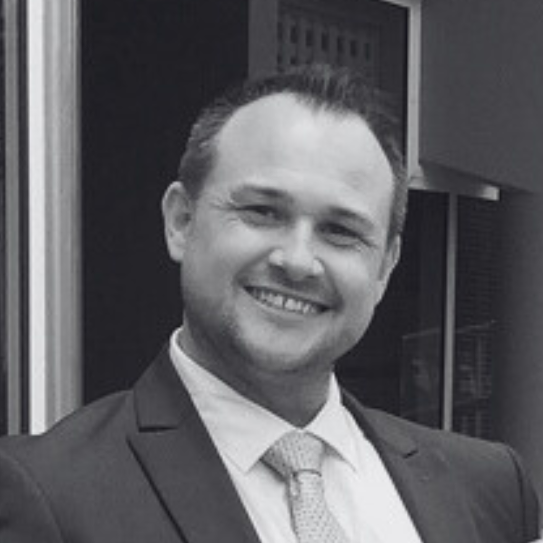 Black and white photo of Ken smiling. He wears a suit and tie.