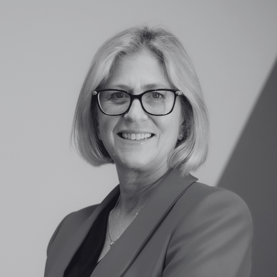 Headshot of Melanie Noden smiling. She has blonde, shoulder-length hair, glasses, and is wearing a blazer.