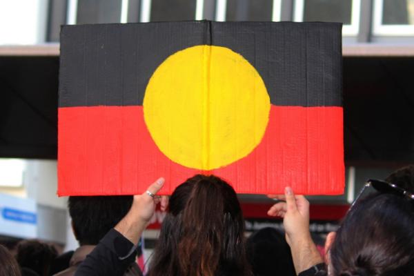 A person holding a painted sign with the Aboriginal flag.