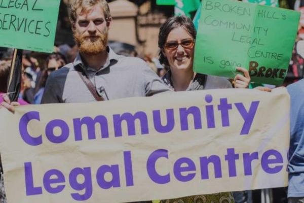Person with a beard holding a large banner that reads 'Community legal centre' in large purple type.