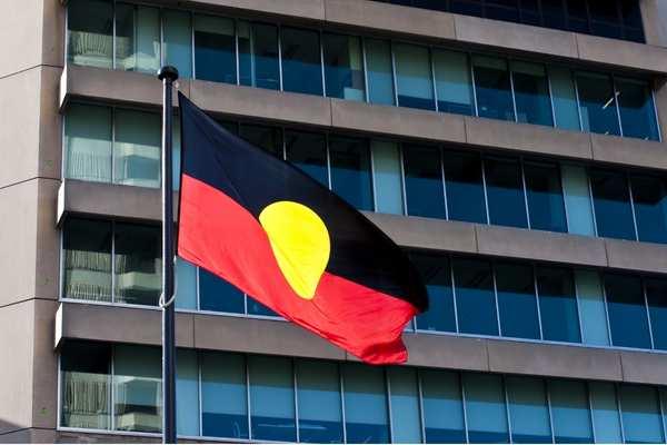 Aboriginal flag flying on a pole in front of a skyrise building.