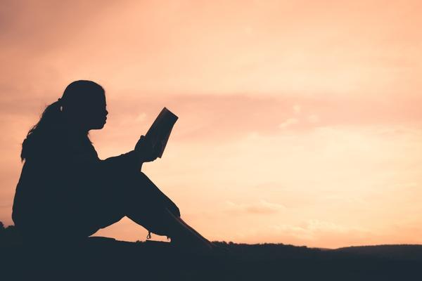 Silhouette of a woman reading a book at sunset.