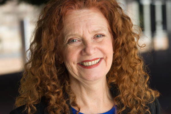 Photo of Robyn Ayres smiling. She has long, red curly hair and is wearing a blue top and black blazer.