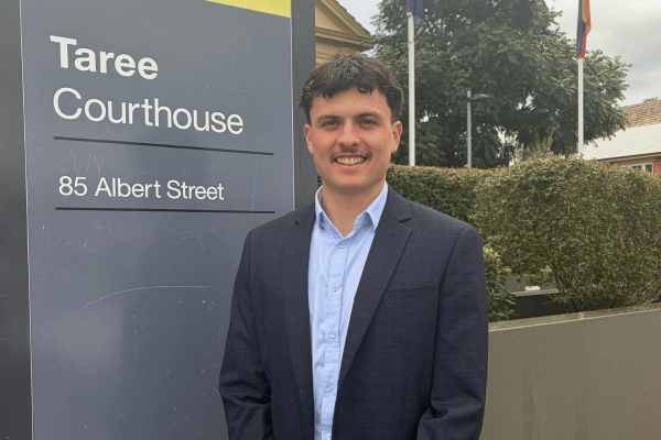 Zaiden smiling outside the Taree Courthouse sign. He wears a blue suit.